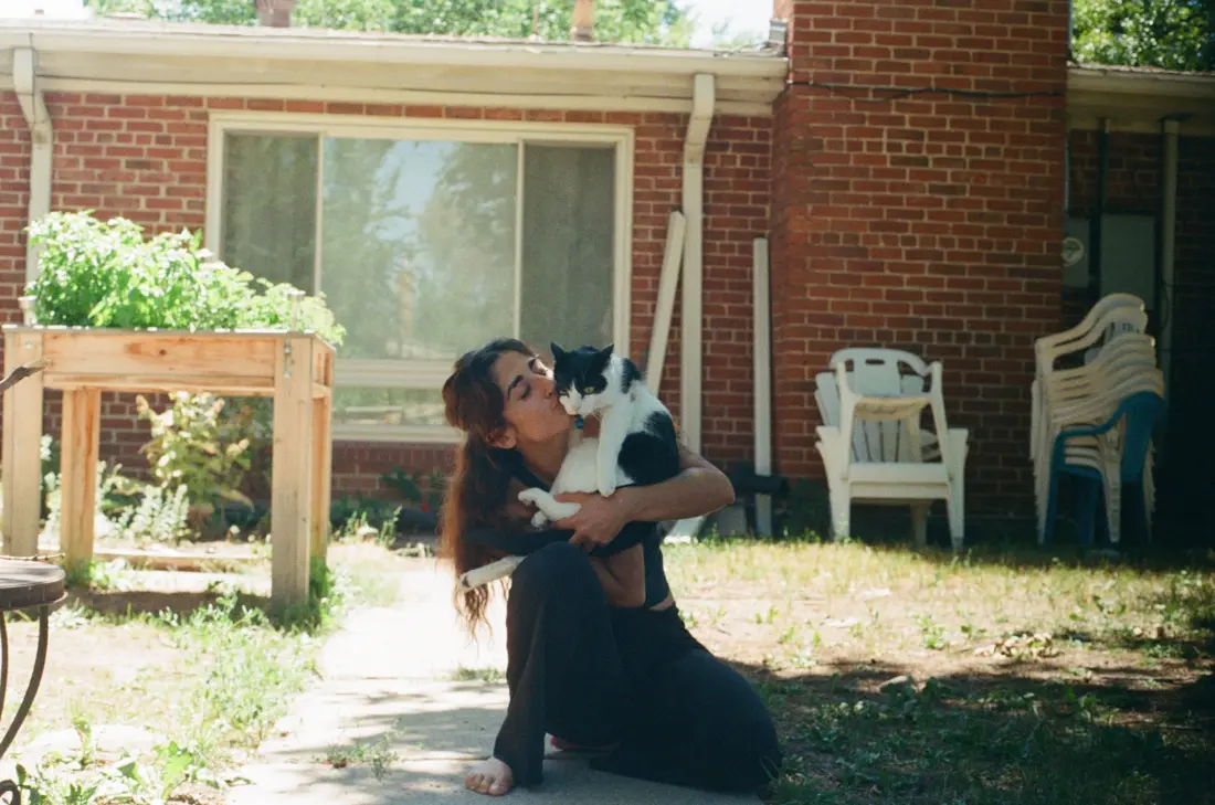 Lara kissing her black and white cat, Theo, in a sunny backyard